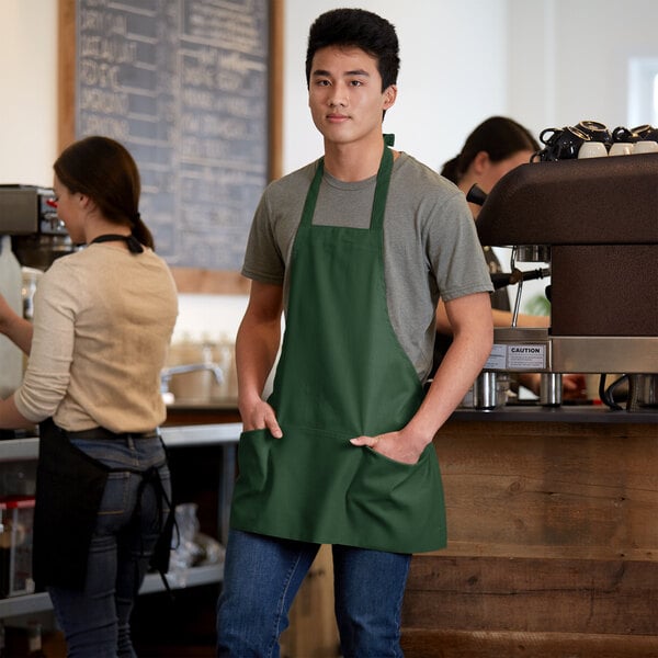 A man wearing a Choice hunter green bib apron with 3 pockets.