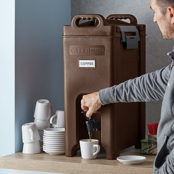 A man using a CaterGator insulated beverage dispenser to fill a coffee machine with a white mug.