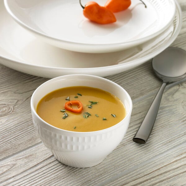 A Libbey Royal Rideau white porcelain bouillon bowl filled with soup with a chili pepper slice on a plate.