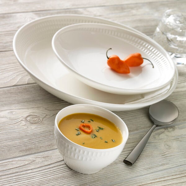 A bowl of soup and a spoon on a Libbey deep coupe plate.