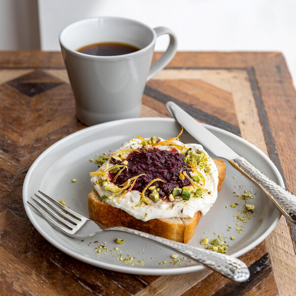 A Libbey Englewood porcelain mug filled with coffee on a table with a plate of food.