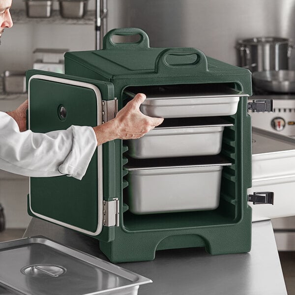 A man in a white shirt and green chef's coat opening a green CaterGator front loading food pan carrier.
