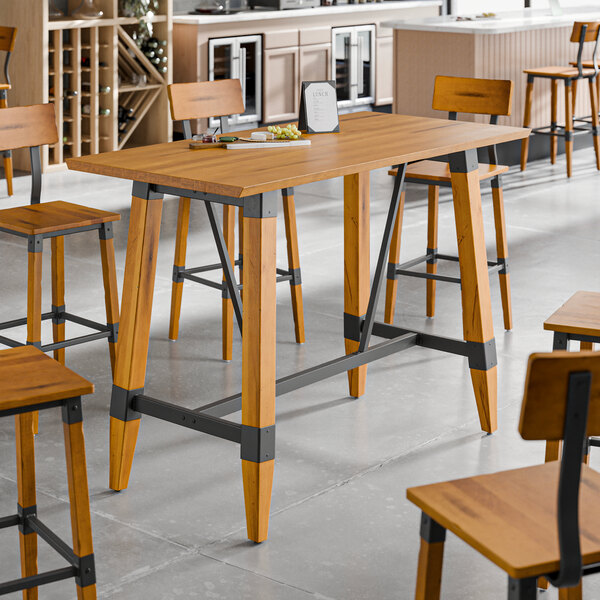 A bar height trestle table with a honey maple finish and industrial metal accents, designed for 30" x 60" table tops.