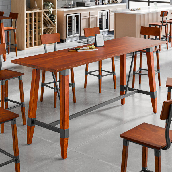 A bar height trestle table with a rustic mahogany finish and industrial metal accents, designed for 30" x 96" table tops.