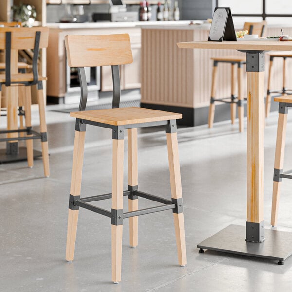 A Lancaster Table & Seating industrial bar stool with a metal frame and wooden legs at a table in a restaurant.