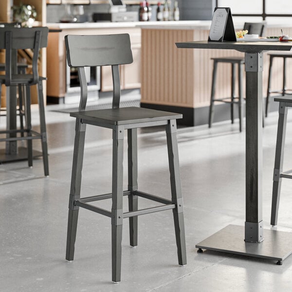 A Lancaster Table & Seating industrial bar stool with a slate gray metal base and wooden seat.