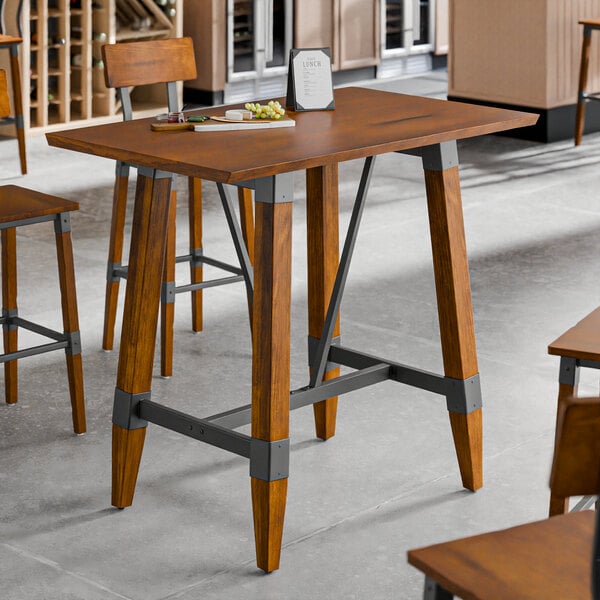 A bar height trestle table with a rustic walnut finish and industrial metal accents, designed for 30" x 48" table tops.