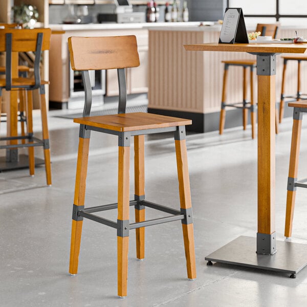 A Lancaster Table & Seating industrial bar stool with a honey maple finish and a metal frame and back.