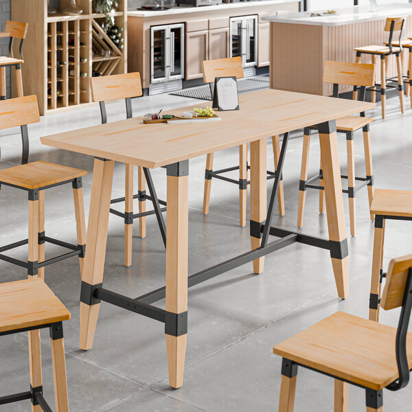 A bar height trestle table with a bleached oak finish and black metal supports, designed for 30" x 72" table tops.