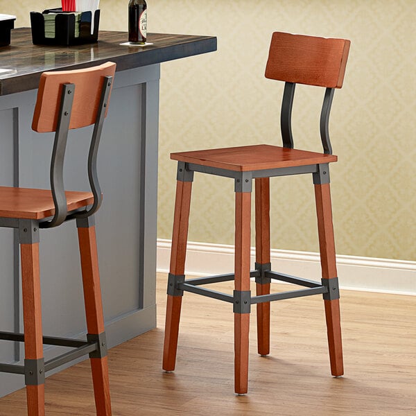 A Lancaster Table & Seating Industrial Bar Stool with Rustic Mahogany Finish next to a counter.