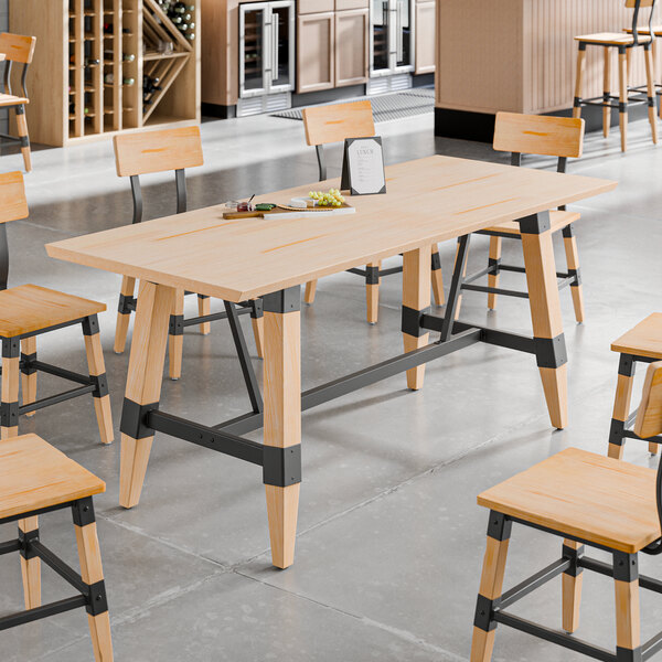 A rectangular solid wood trestle base table with a bleached oak finish and industrial metal accents.