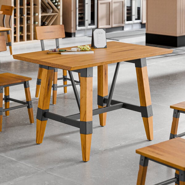 A rectangular solid wood table with a honey maple finish and industrial-style trestle base.