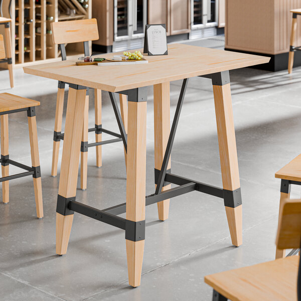 A rectangular bar height table with a solid wood live edge top and trestle base in a bleached oak finish, featuring metal support accents.