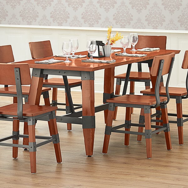 A Lancaster Table & Seating Industrial solid wood trestle table with wine glasses and chairs.