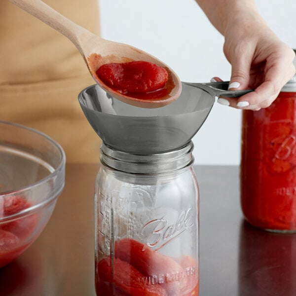 Person funneling tomatoes into a canning jar