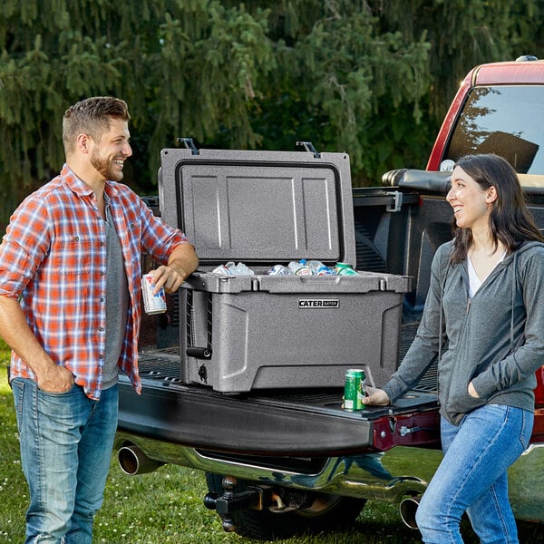 A man and woman standing next to a CaterGator outdoor cooler full of soda cans.