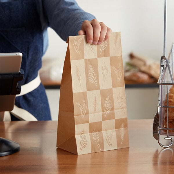 A person holding a brown Bagcraft paper bag with wheat design on it.