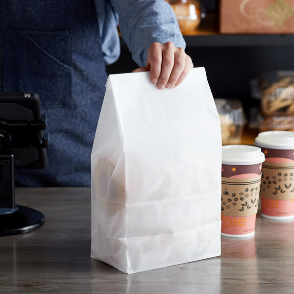 A person holding a Bagcraft white bag with a piece of bread inside.