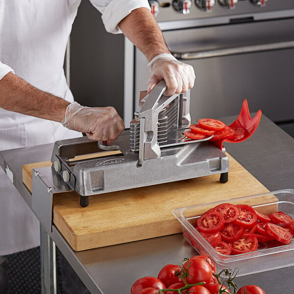 A man using a Prince Castle Tomato Saber to slice tomatoes on a cutting board.