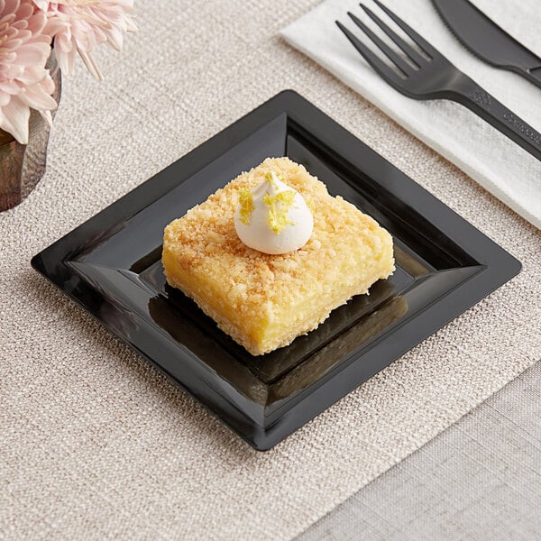 A square black WNA Comet Milan Grand plastic dessert plate with a square yellow dessert with white frosting on top.