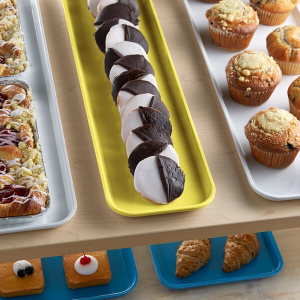 A yellow Cambro market tray of pastries on a table in a bakery display.