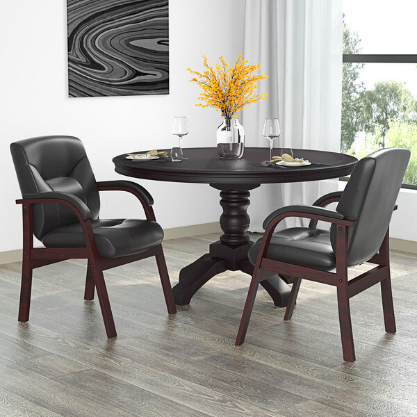 A Boss black leather guest chair next to a table with a vase of yellow flowers.