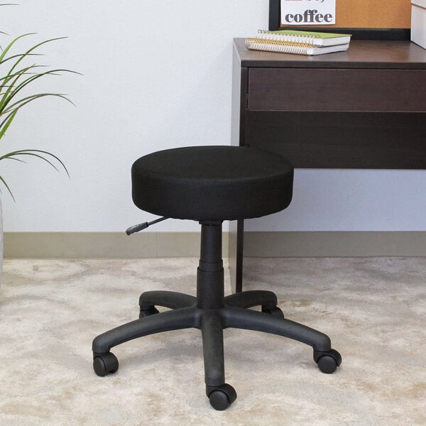 A Boss black mesh DOT stool with wheels sitting in front of a desk.