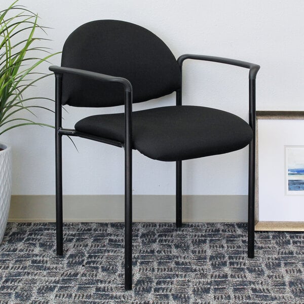 A Boss Diamond Black stacking chair with arms next to a plant in a white planter.