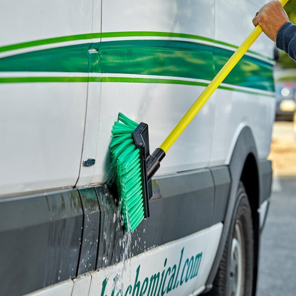 A person cleaning a vehicle with a green and yellow Carlisle Flo Thru brush.