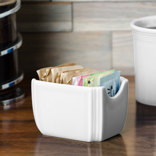 A white ceramic Fiesta sugar caddy on a counter with packets inside.