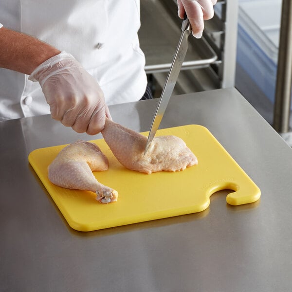 chef wearing disposable cloves and cutting raw chicken on a yellow cutting board