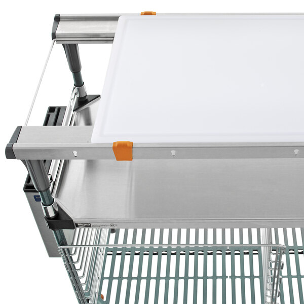 A Metro PrepMate MultiStation with a stainless steel tray and white cutting board on a cart.