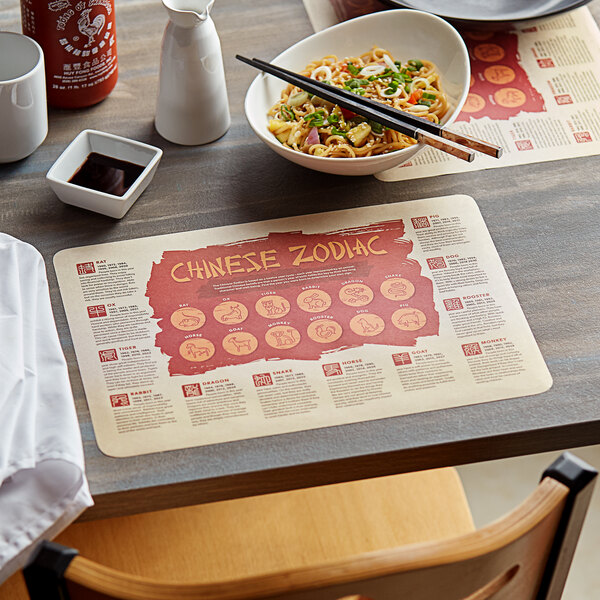 A table with a bowl of noodles and chopsticks on a Choice Chinese Zodiac paper placemat.