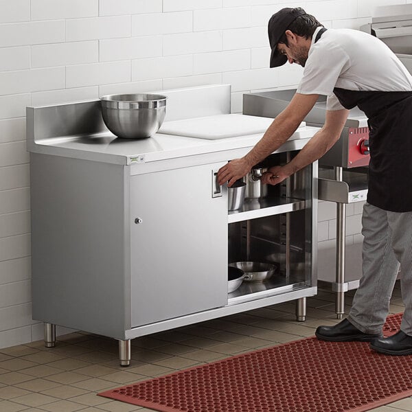 A man in a black apron preparing food on a Regency stainless steel enclosed base table in a professional kitchen.