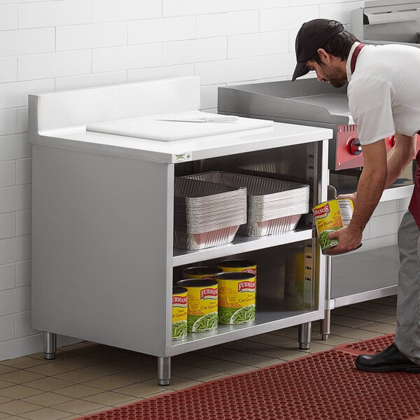 A man putting food on a stainless steel work table with an enclosed base.