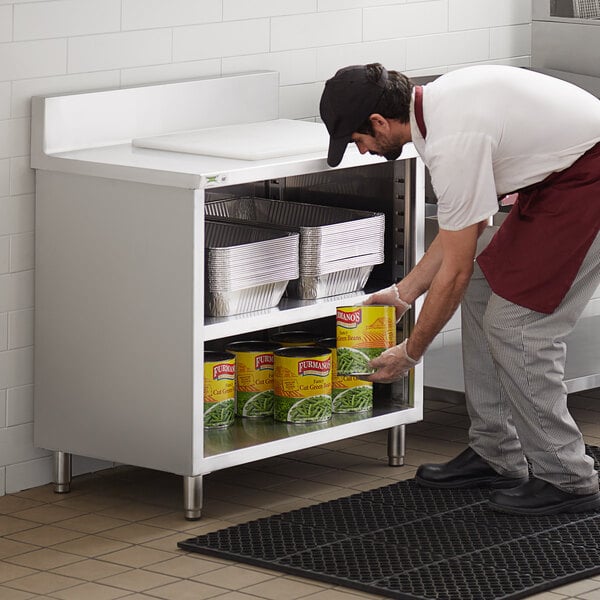 A man putting cans of food on a Regency stainless steel enclosed base table with a shelf.