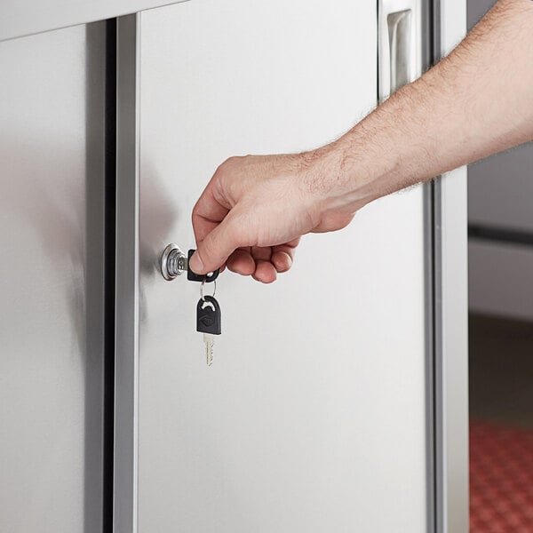 A hand using a key to open a door on a Regency stainless steel enclosed base table.