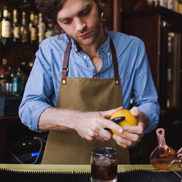 A man in a Hardmill Field Tan Waxed Canvas apron squeezing an orange over a drink.