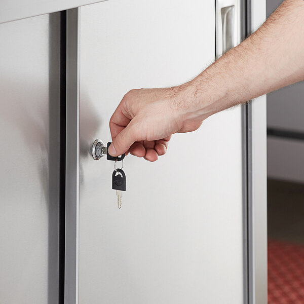 A hand using a key to open a door on a Regency stainless steel enclosed base table