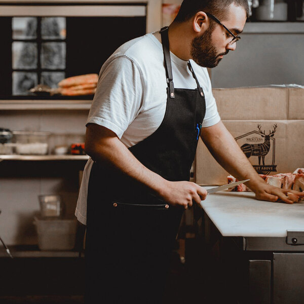 A man in a Hardmill black apron cutting meat on a counter.