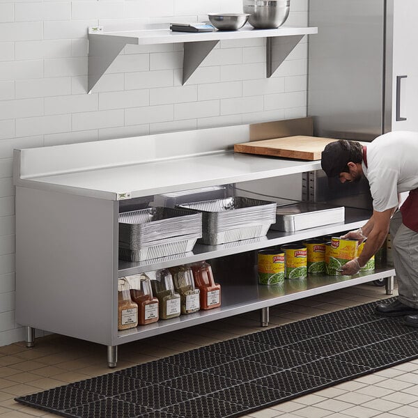 A man in a white shirt and white apron putting food onto a shelf on a Regency stainless steel table.