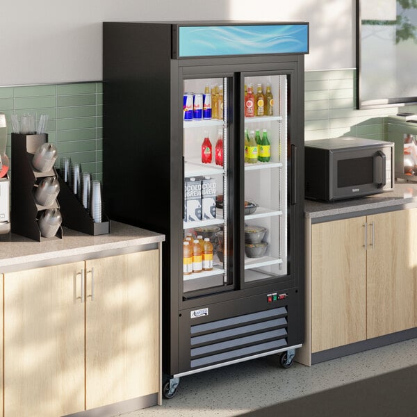 A black sliding glass door merchandiser refrigerator with LED lighting, stocked with beverages and food items.
