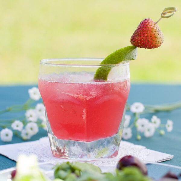 A Libbey Chivalry old fashioned glass with a cocktail and a lime wedge on a doily.