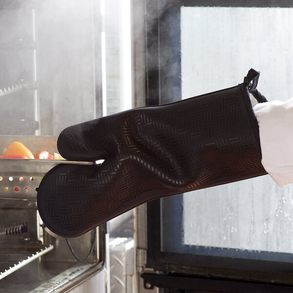 A person wearing a black San Jamar Flexguard silicone oven mitt.