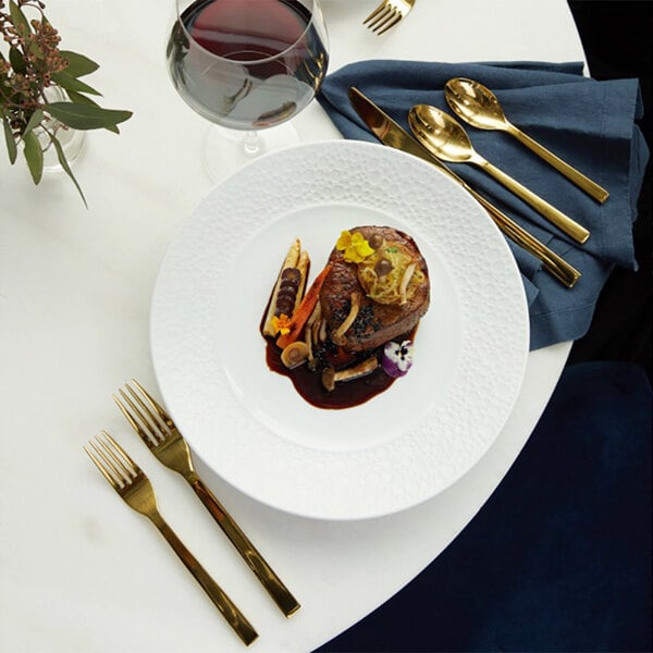 A plate of food with a Oneida stainless steel dinner knife next to a gold spoon.