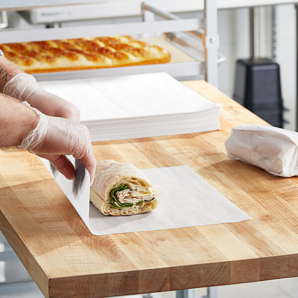 A person cutting a sandwich on a rectangular cutting board.