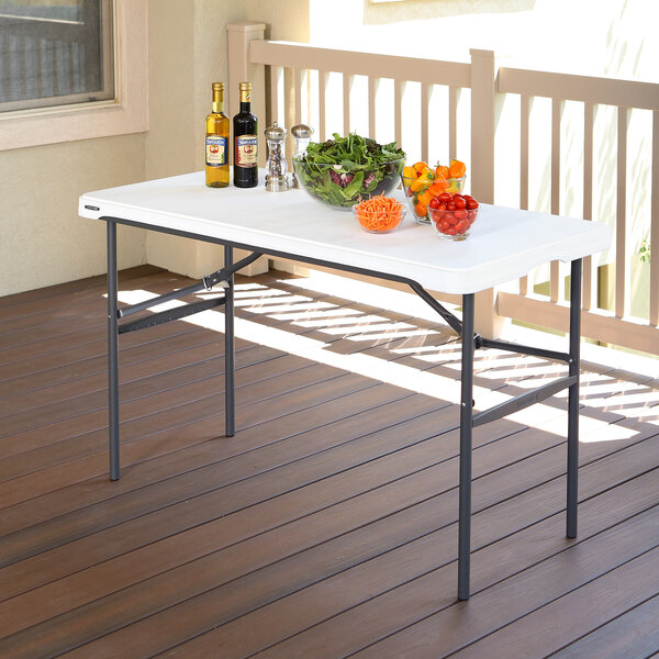 A Lifetime white plastic folding table on a patio with bowls of salad, peppers, and tomatoes.