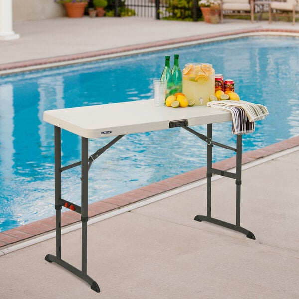 A Lifetime almond plastic folding table with drinks and bottles on it by a pool.