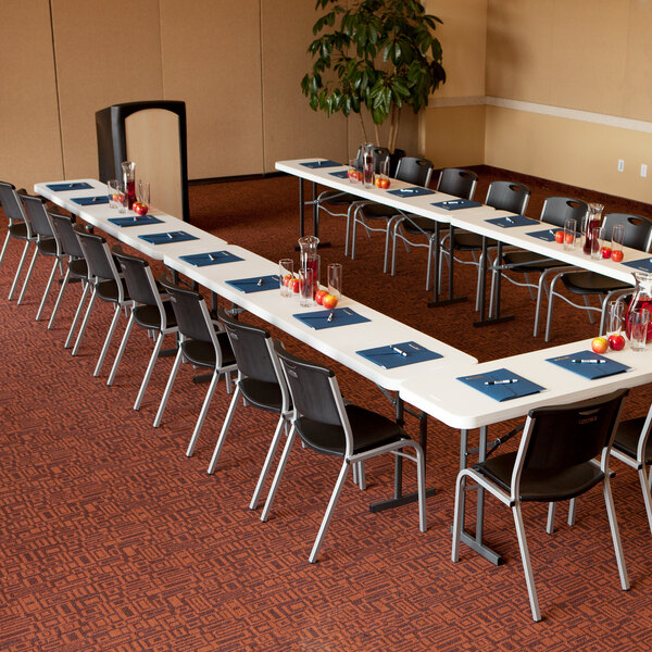 A long white Lifetime plastic seminar table with black chairs and glasses on it.