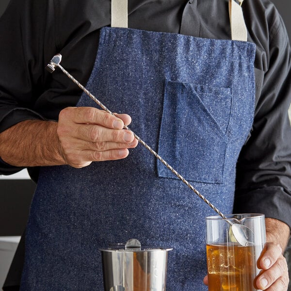 A man in an apron using an Arcoroc by Chris Adams Hammer Bar Spoon to stir a drink in a glass.